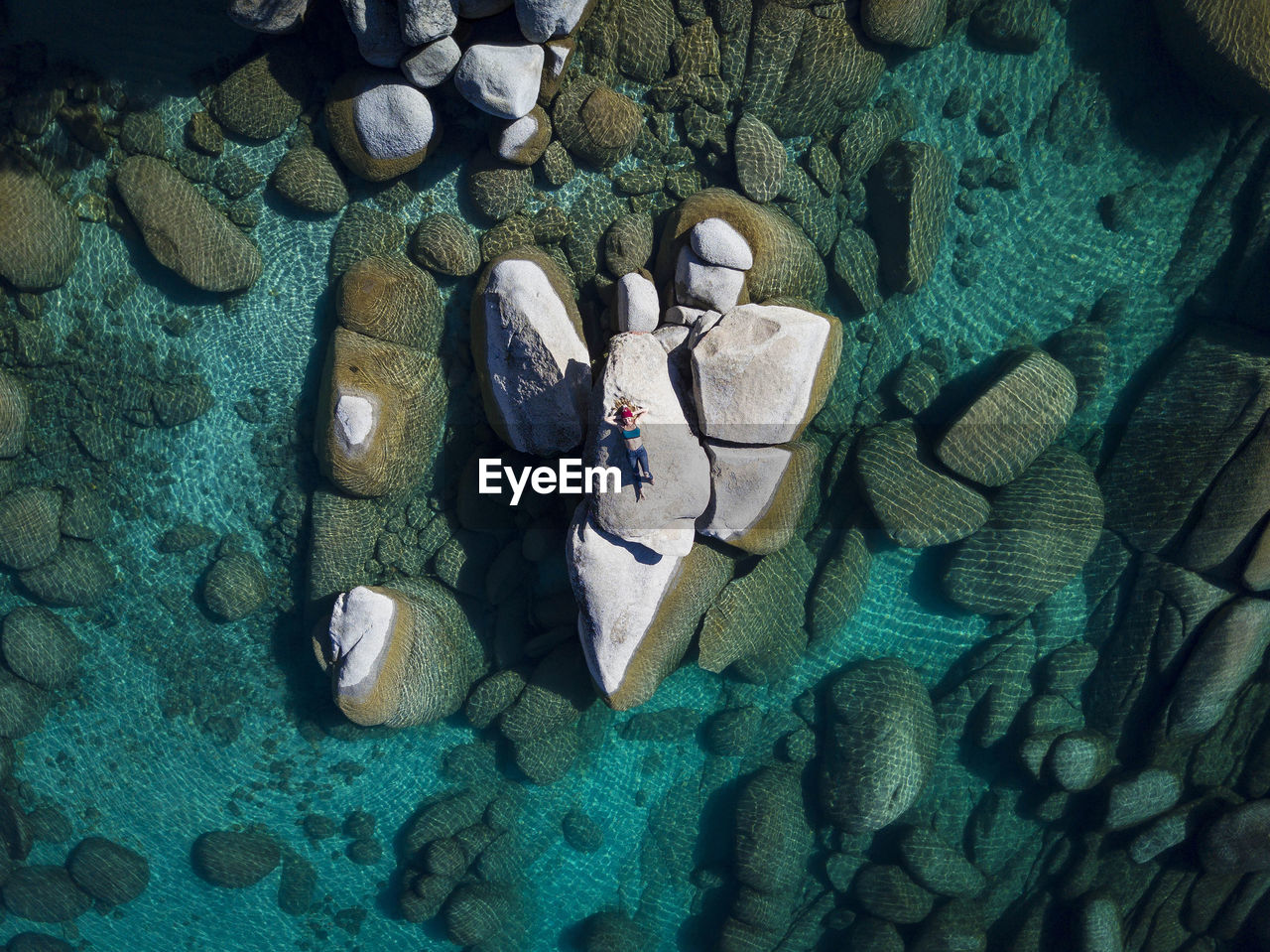 Drone shot of woman relaxing on rock at lake tahoe on sunny day