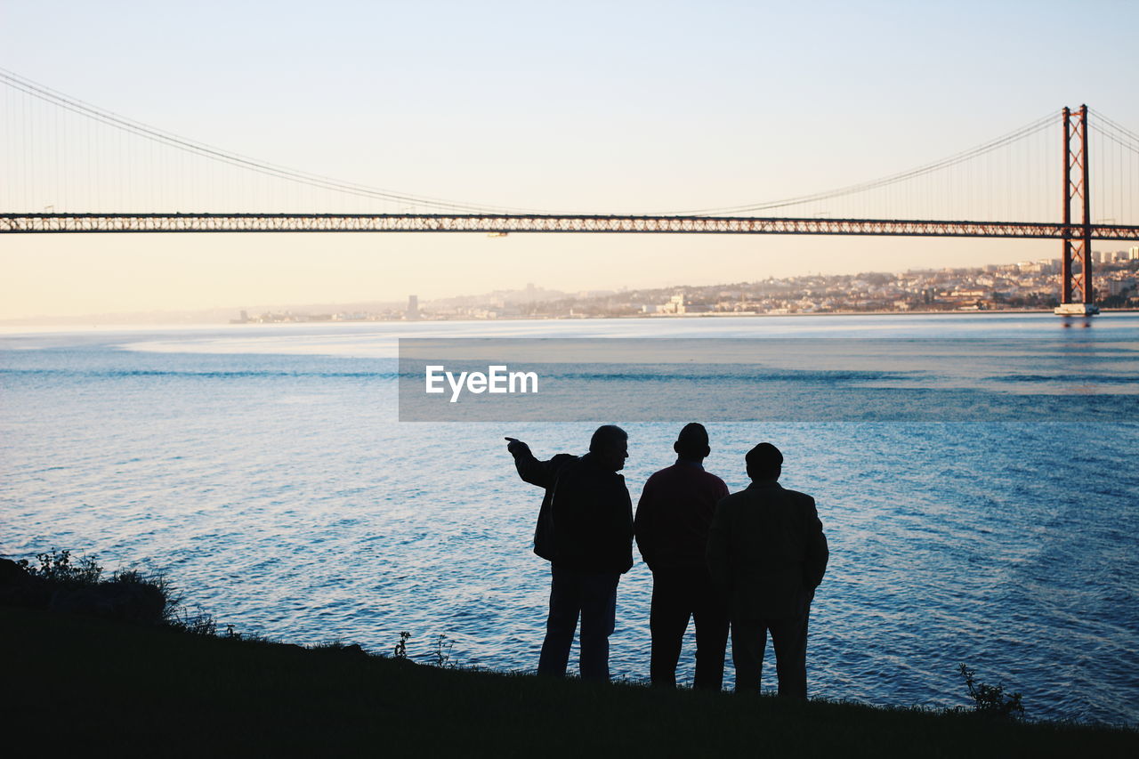 Silhouette male friends standing together by sea against sky