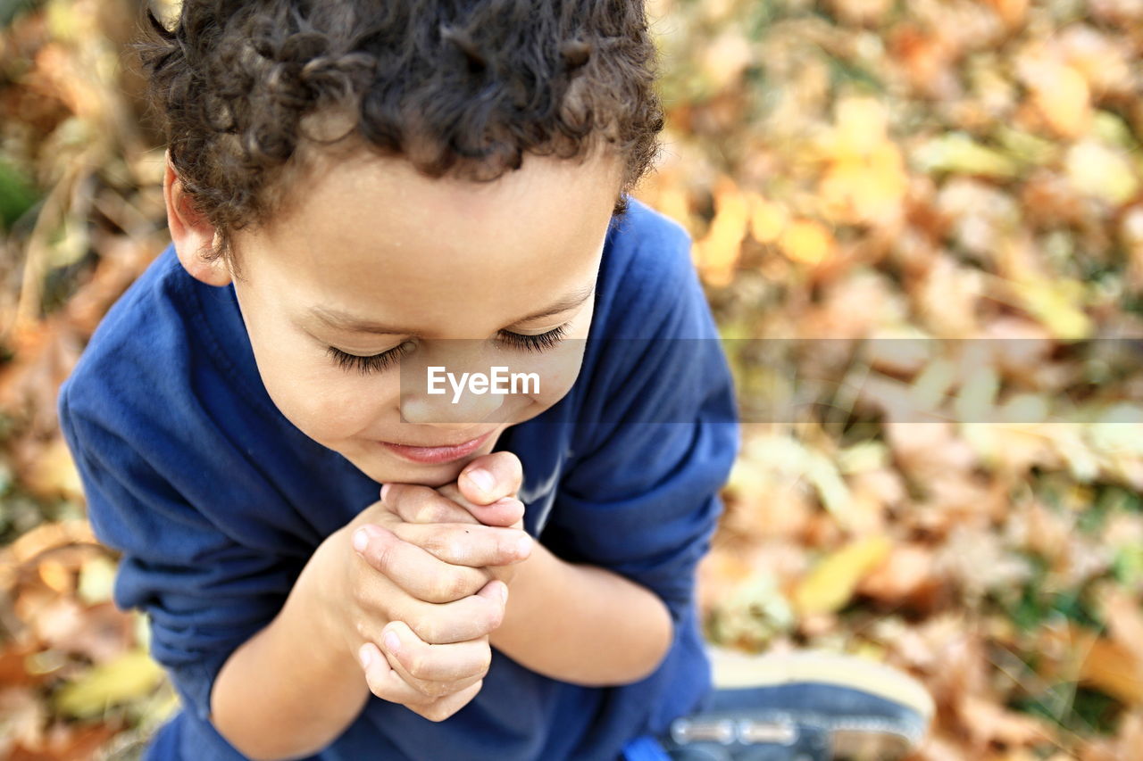 High angle view of cute boy with eyes closed and hands clasped praying in park during autumn