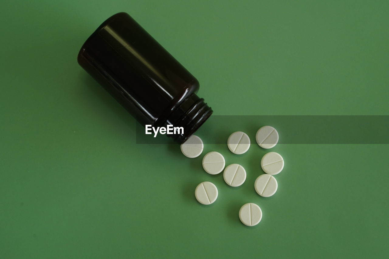 Close-up of pills spilling from bottle against green background