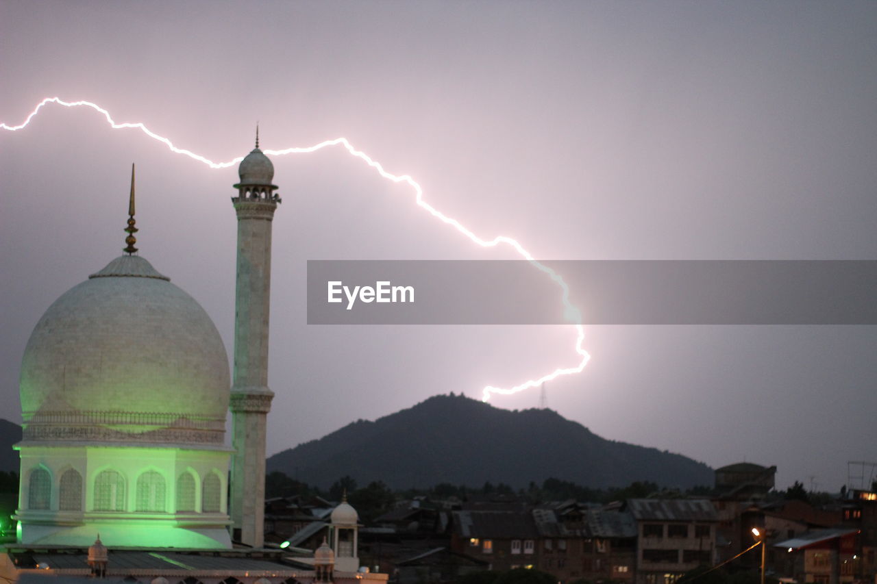 Low angle view of mosque against lightning on hill at night