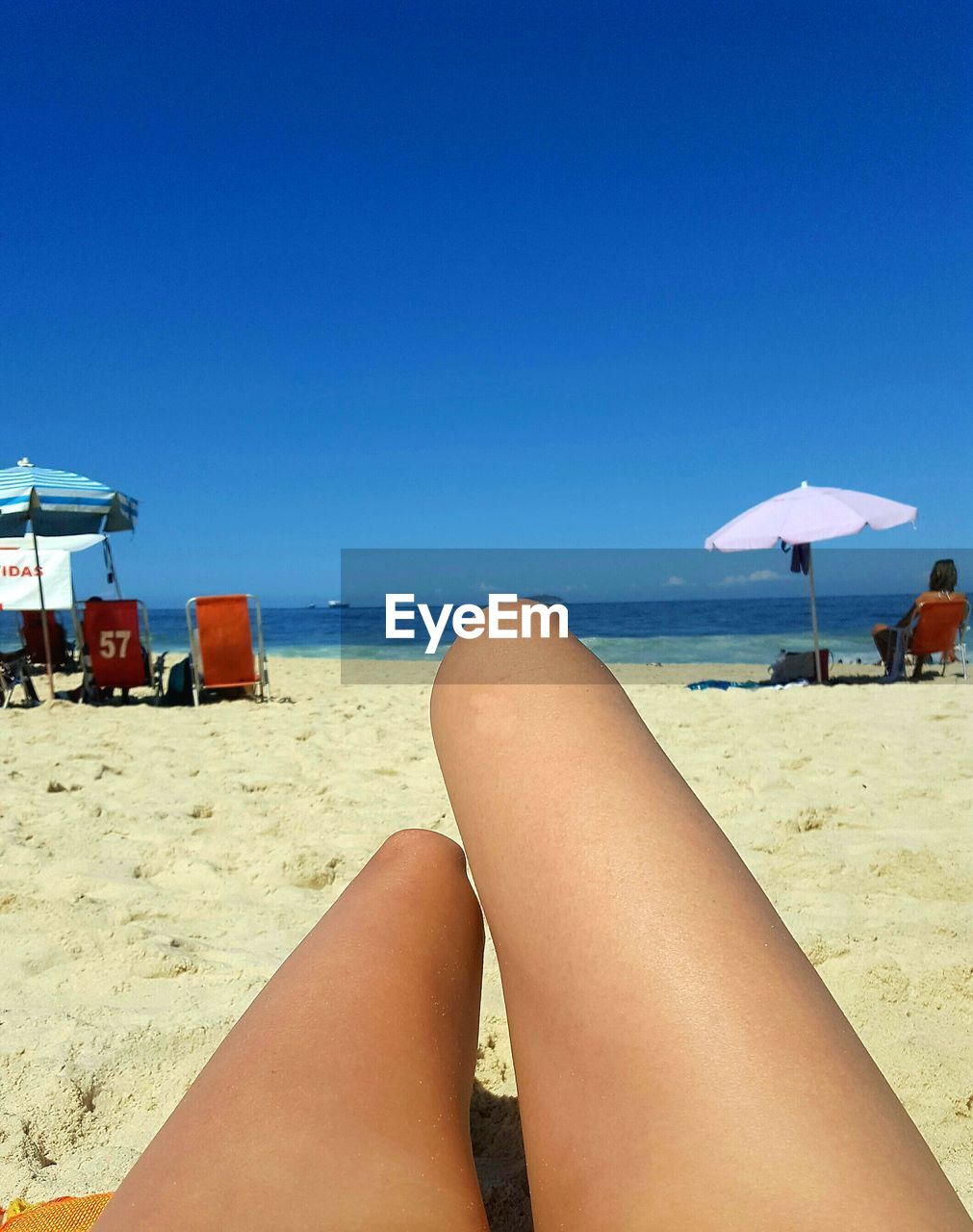 LOW SECTION OF WOMAN RELAXING ON BEACH AGAINST CLEAR SKY