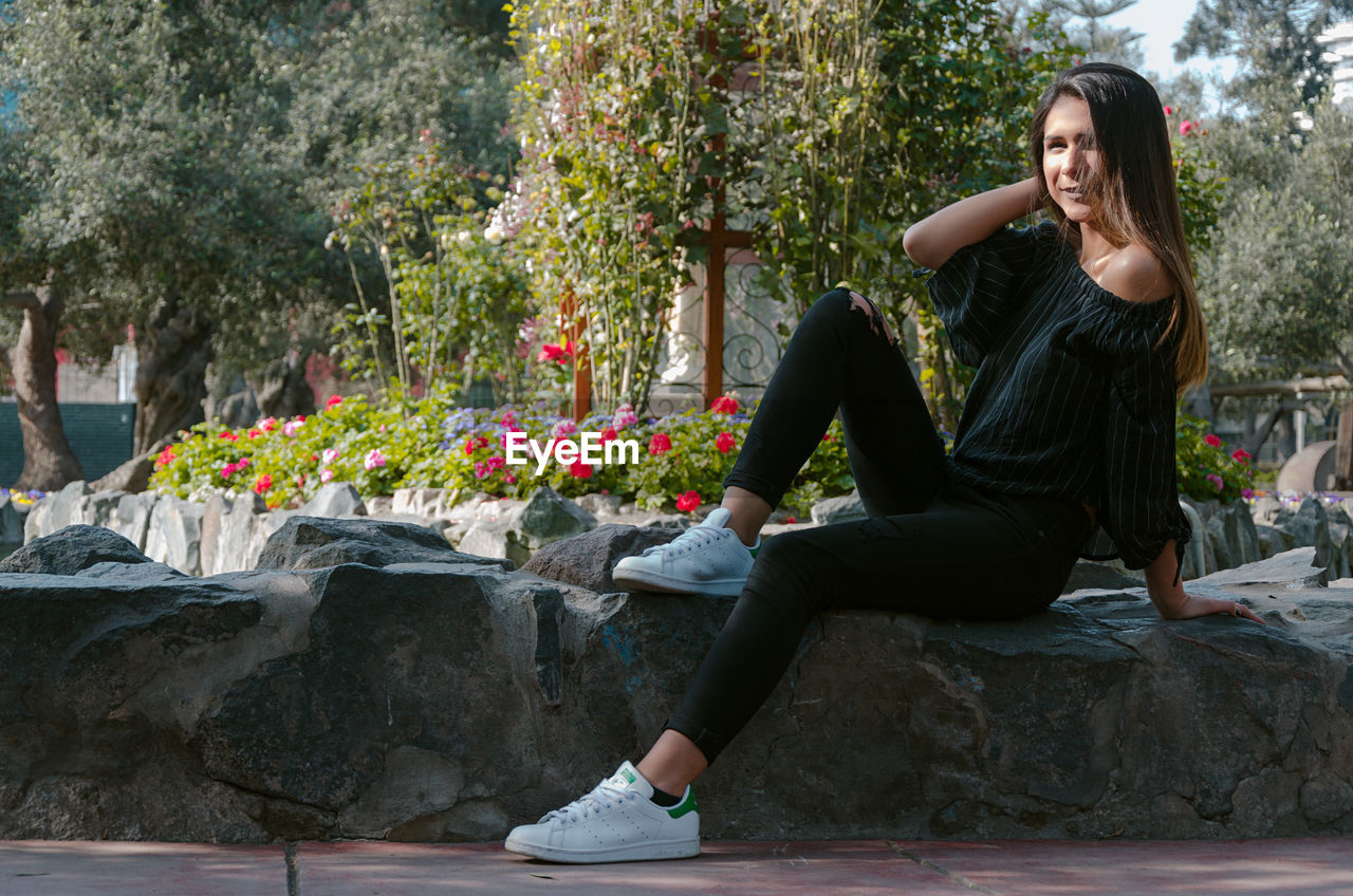 FULL LENGTH OF WOMAN SITTING BY FLOWER TREES