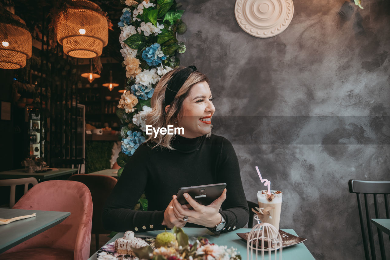 WOMAN LOOKING AT CAMERA WHILE SITTING IN RESTAURANT