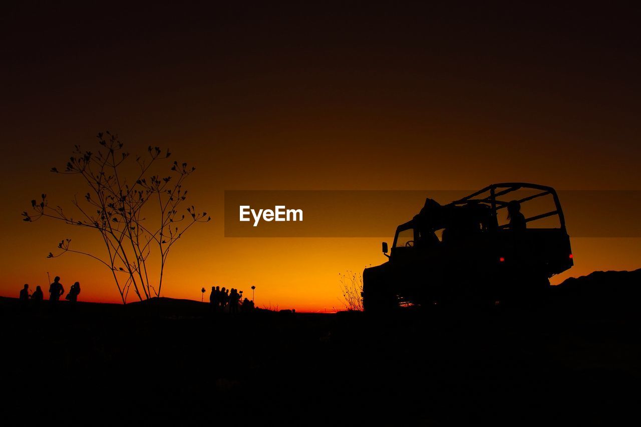 Silhouette people and vehicle against sky at sunset