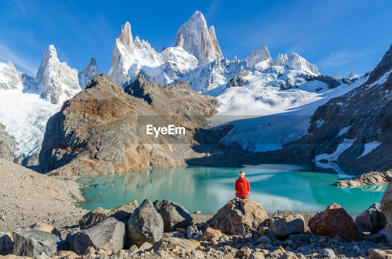 Rear view of person sitting on rock against sky during winter