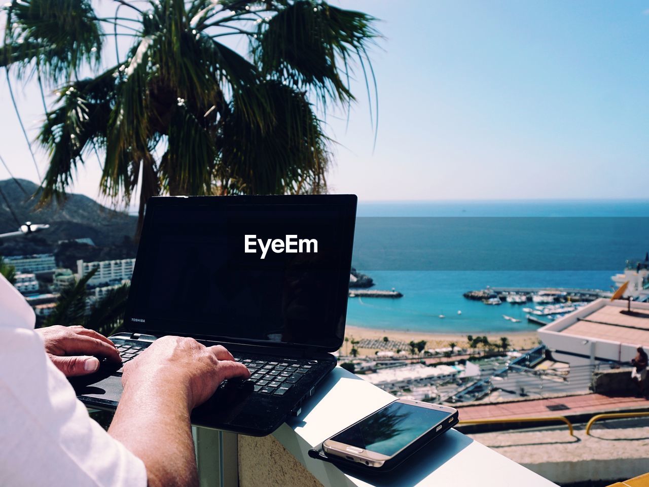 Cropped image of person using laptop by smart phone on sunny day