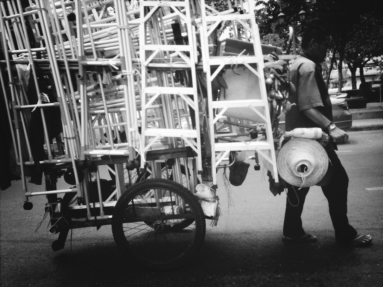 Side view of man pulling cart with ladders on street