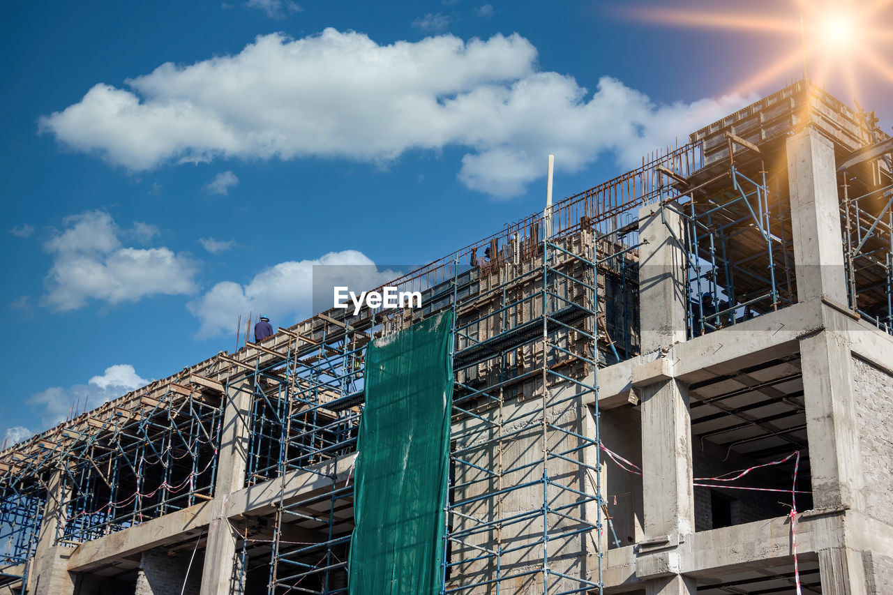 LOW ANGLE VIEW OF BUILDING BY CONSTRUCTION AGAINST SKY