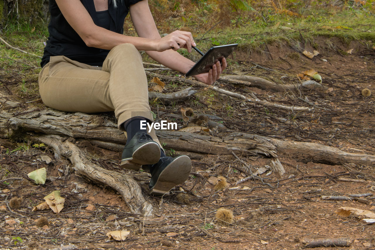 Low section of woman with digital tablet sitting in forest