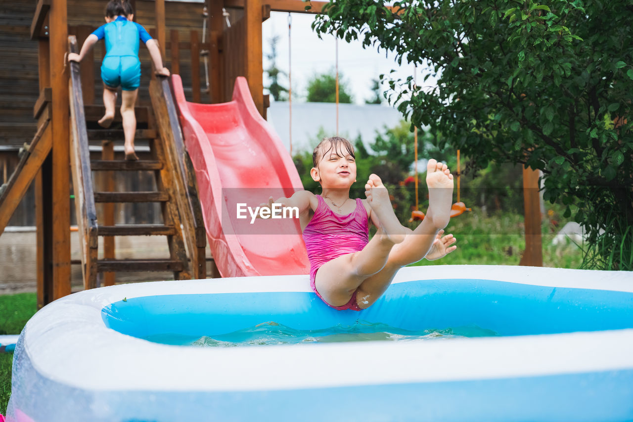 Full length of smiling girl playing on slide in swimming pool