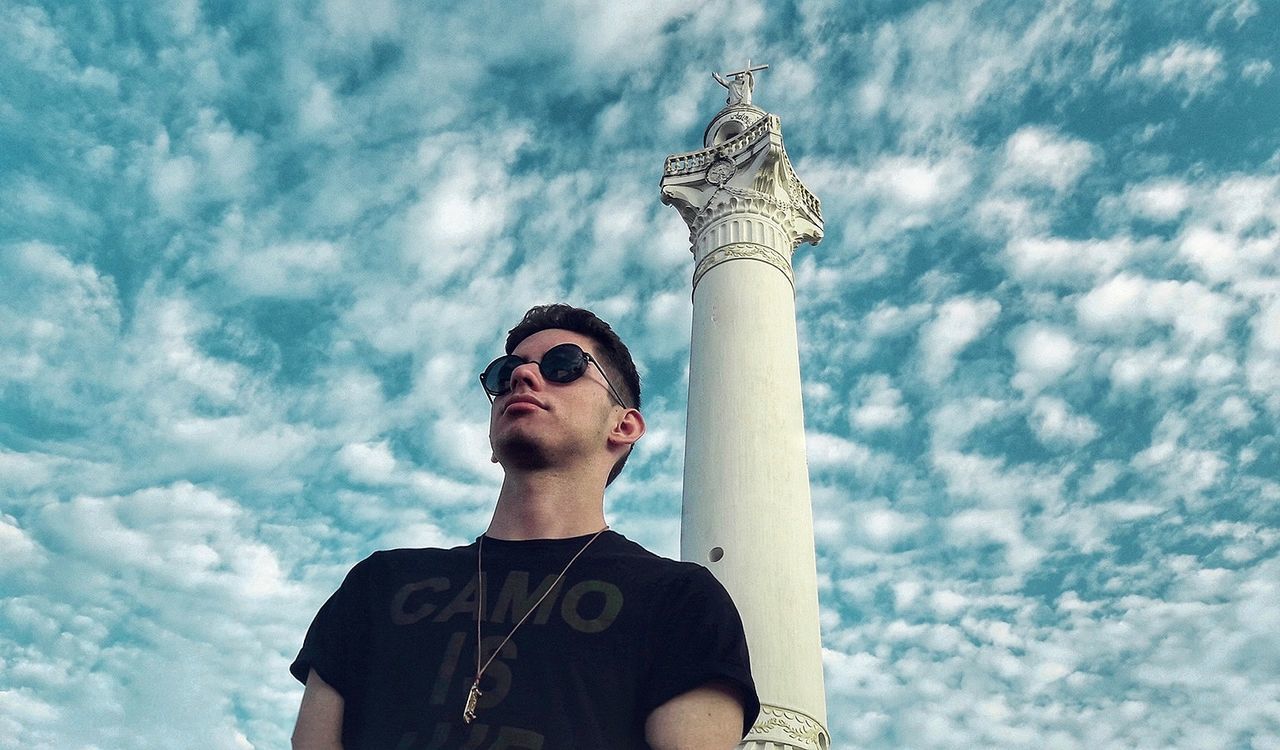 Low angle view of young man and column against cloudy sky