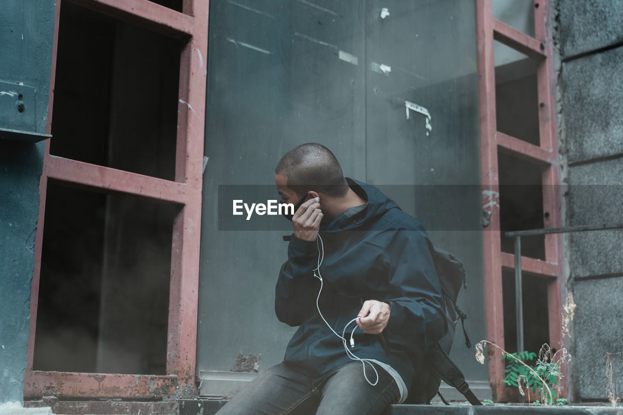 Young man wearing mask listening music while sitting outdoors