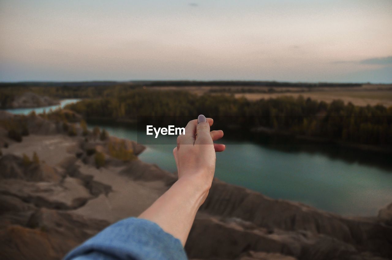 Cropped hand of woman gesturing by lake against sky