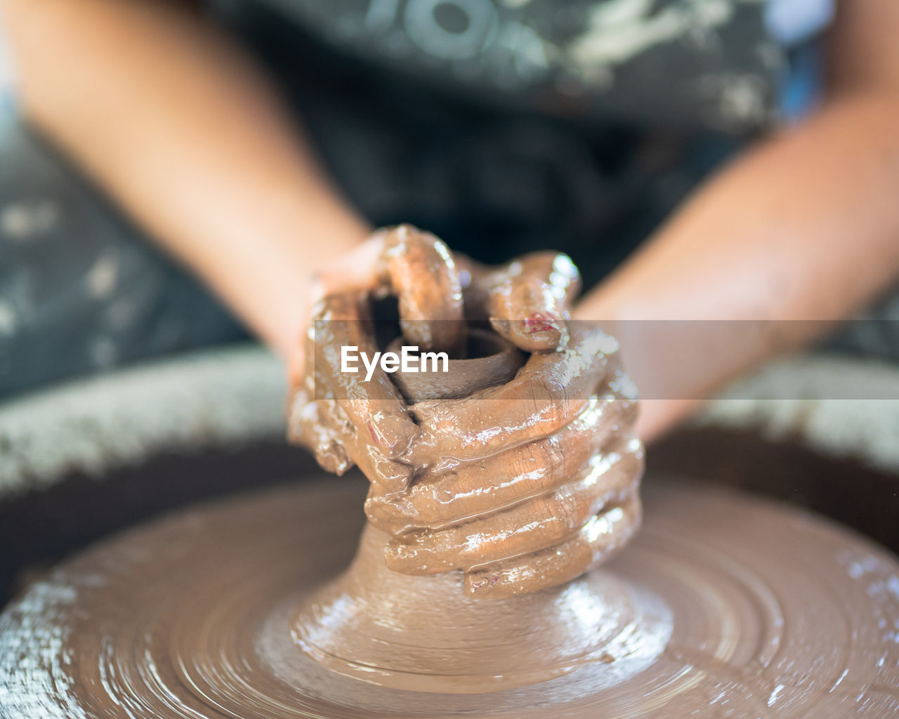 Midsection of woman making pot on pottery wheel