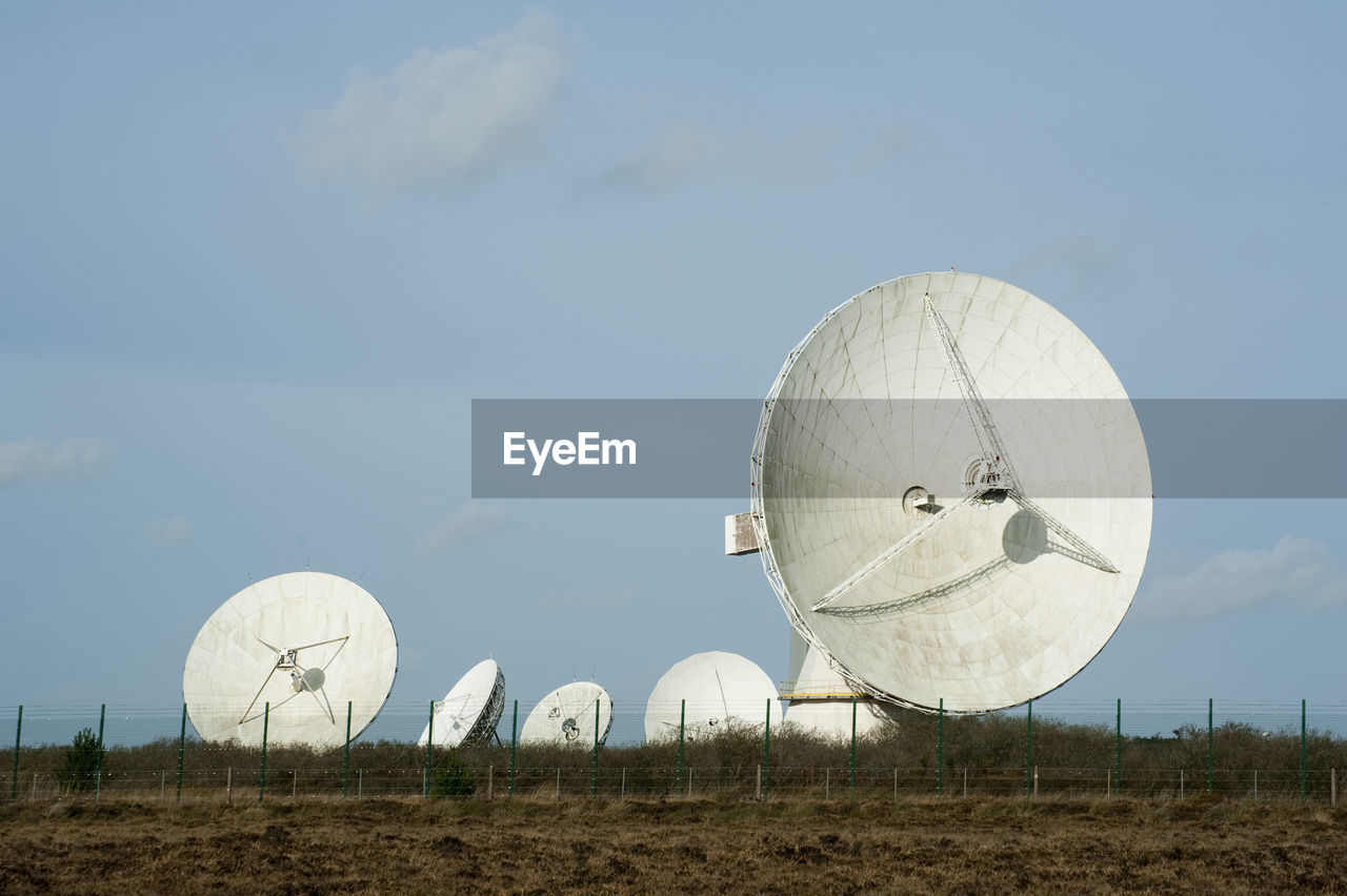 Parabolic satellites on field against sky