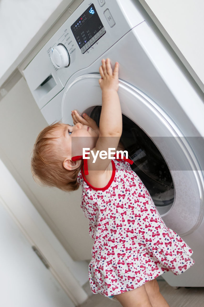 Side view of cute girl standing by washing machine