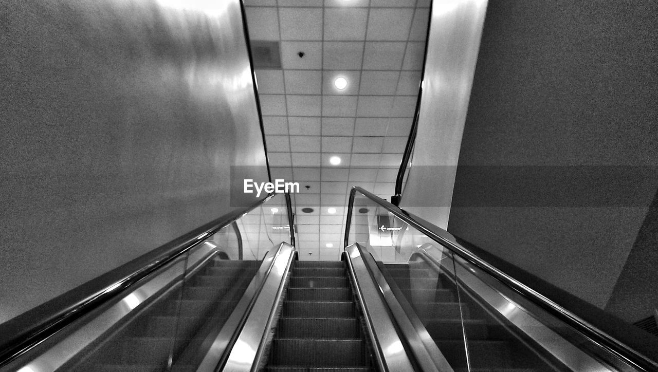 Low angle view of escalator against tiled ceiling
