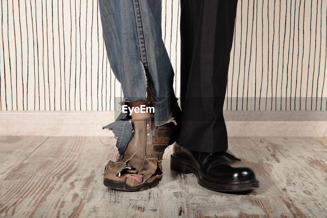 Low section of man wearing torn jeans and pants while standing on floor