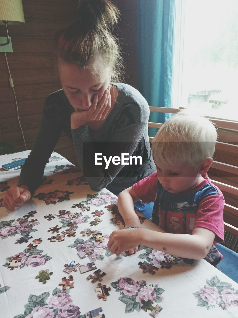 Boy assembling jigsaw puzzle while sitting by mother at table