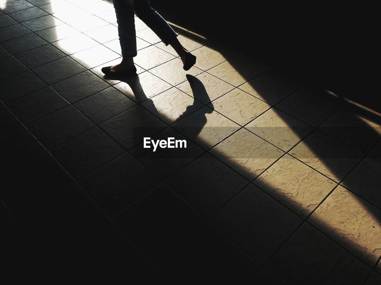 Low section of silhouette woman walking on tiled floor