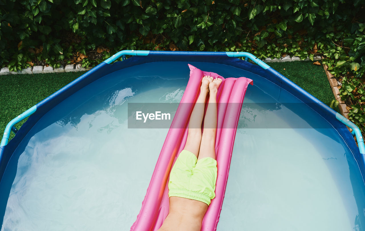 Cenital view of part of a boy lying on a pink float resting in a pool.