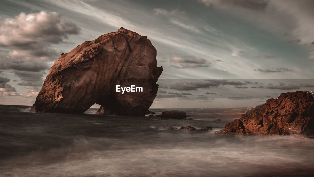 ROCK FORMATION ON SHORE AGAINST SKY