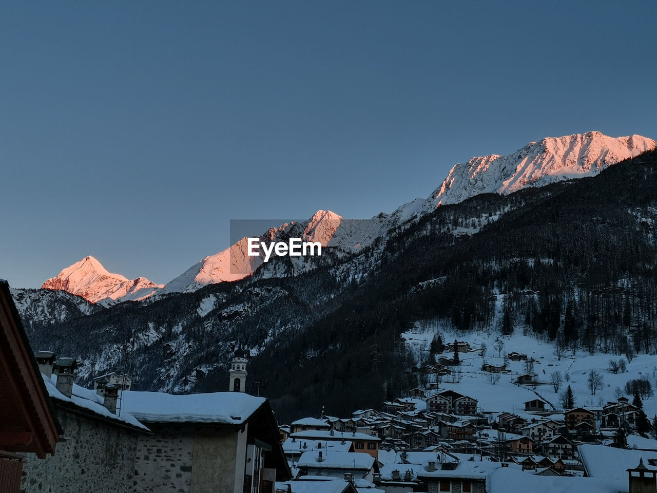 Houses by snowcapped mountains against clear sky during winter