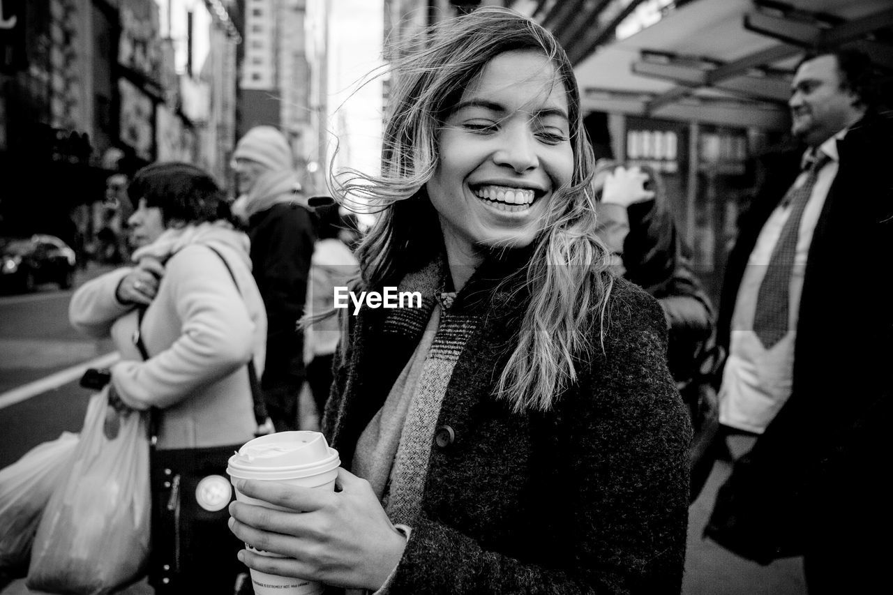 Happy young woman holding drink while walking on city street