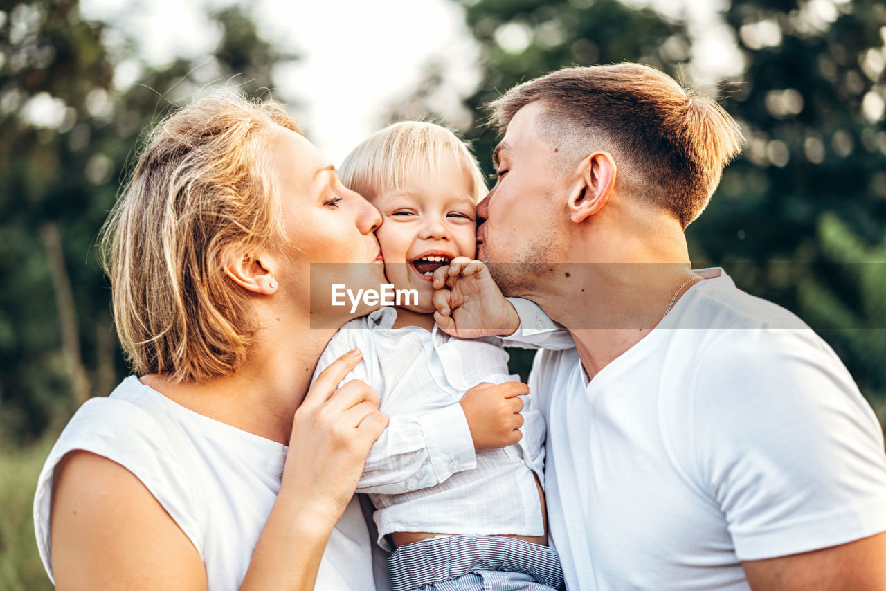 Cheerful mother and father kissing son on field