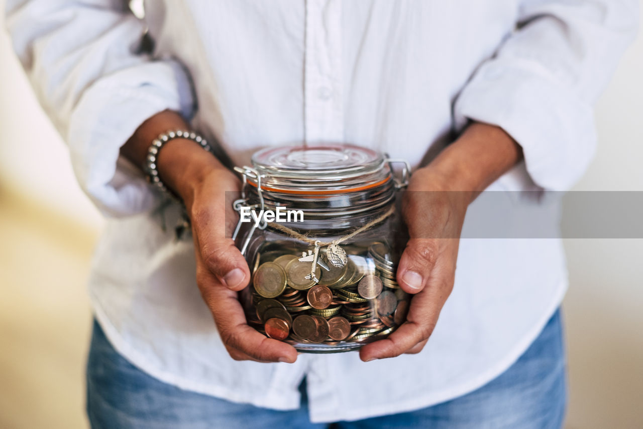 Midsection of woman holding coins in jar at home