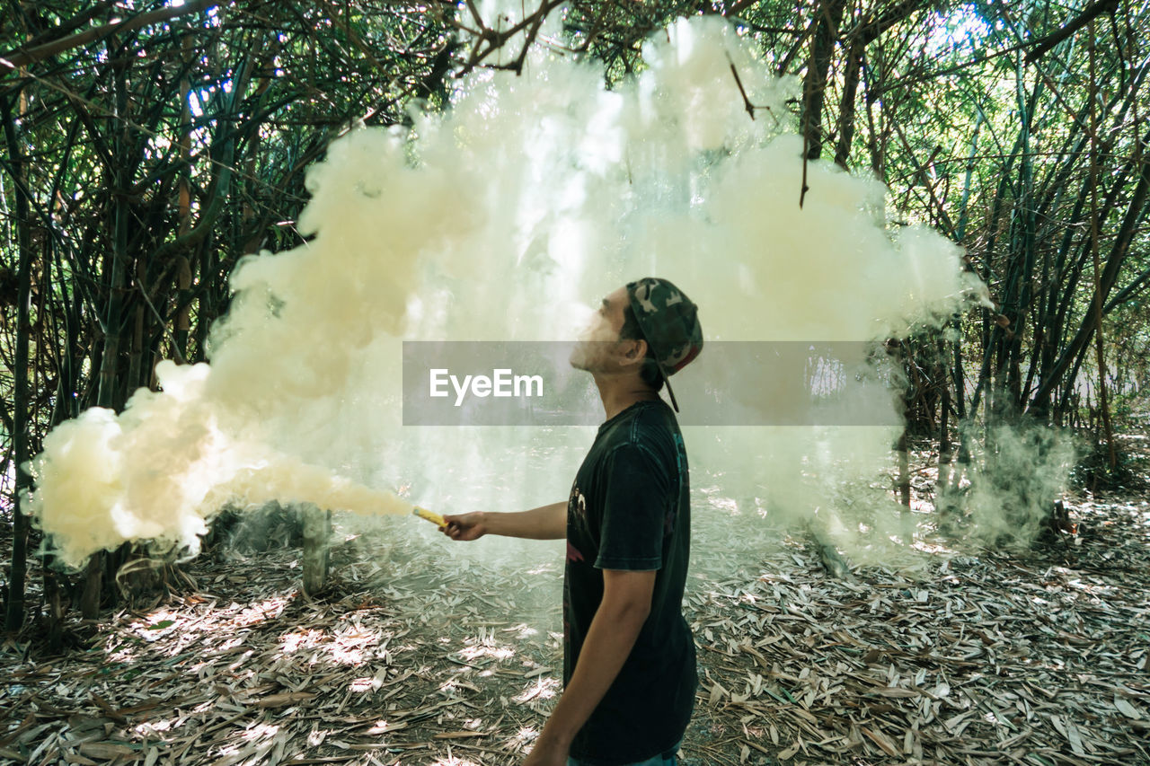 Side view of man holding distress flare while standing at lake