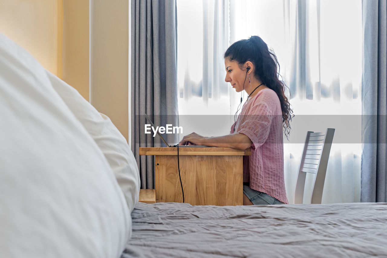 View from behind the bed at smiling woman working at a laptop. always in touch. home office concept. 