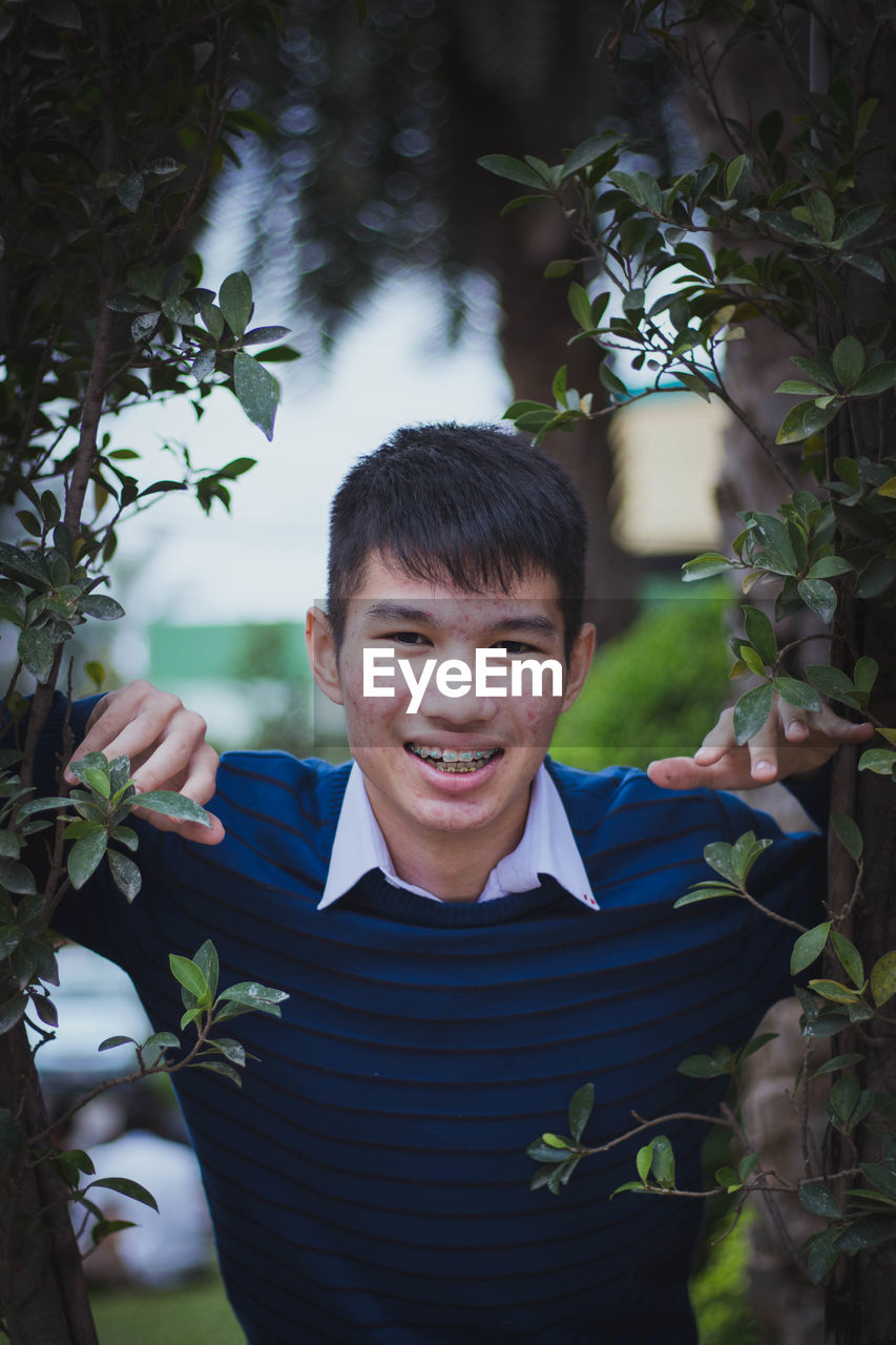 Portrait of smiling teenage boy with braces standing by plants