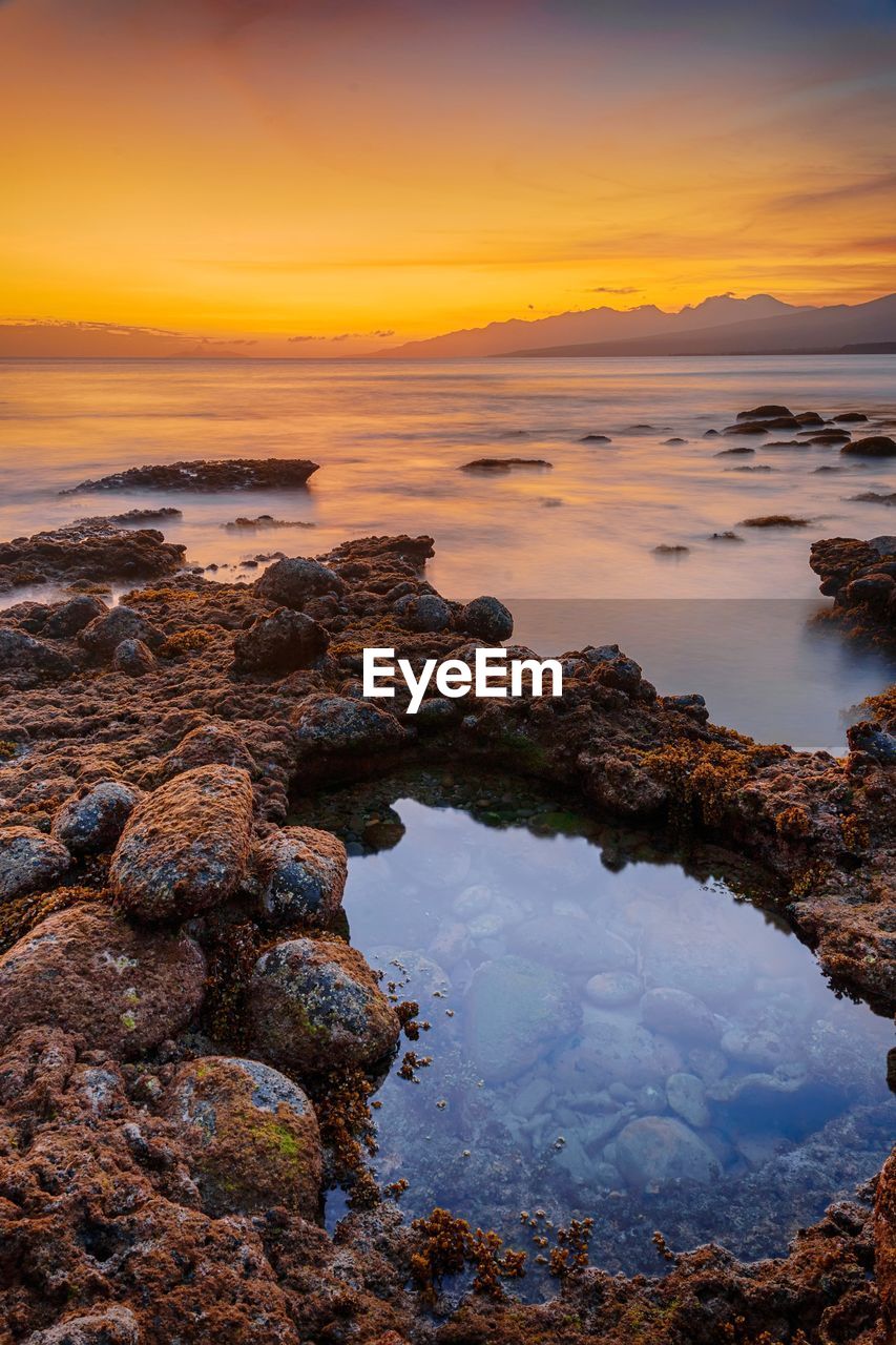 ROCKS BY SEA AGAINST SKY DURING SUNSET