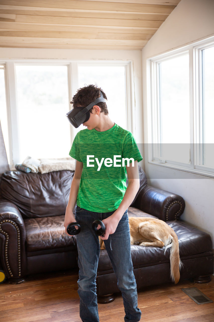 Teen boy playing with vr system with family dog behind him on couch