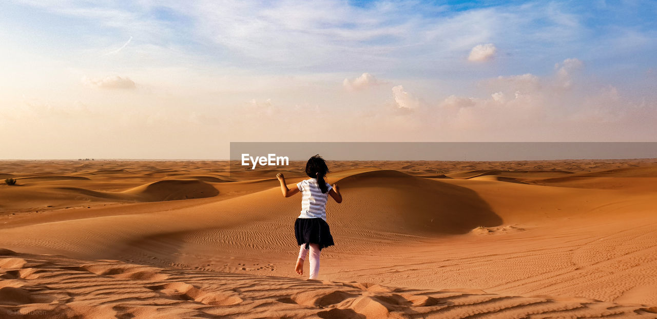 Rear view of girl running in desert against sky during sunset