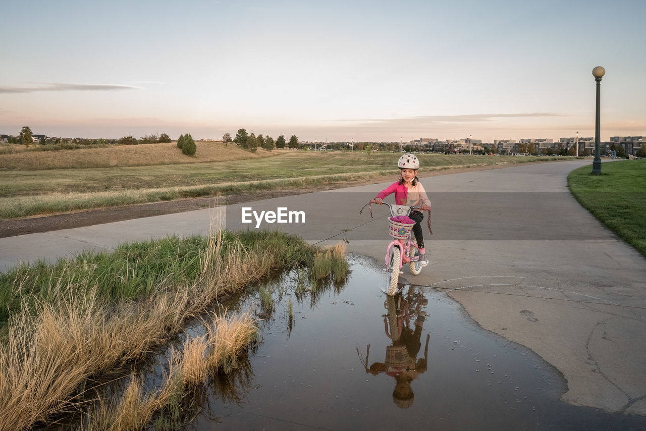 Playful young girl bikes through a puddle of water in a park