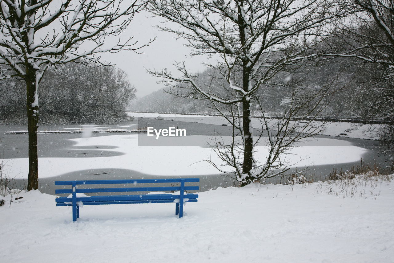 EMPTY BENCH BY SNOW COVERED PARK