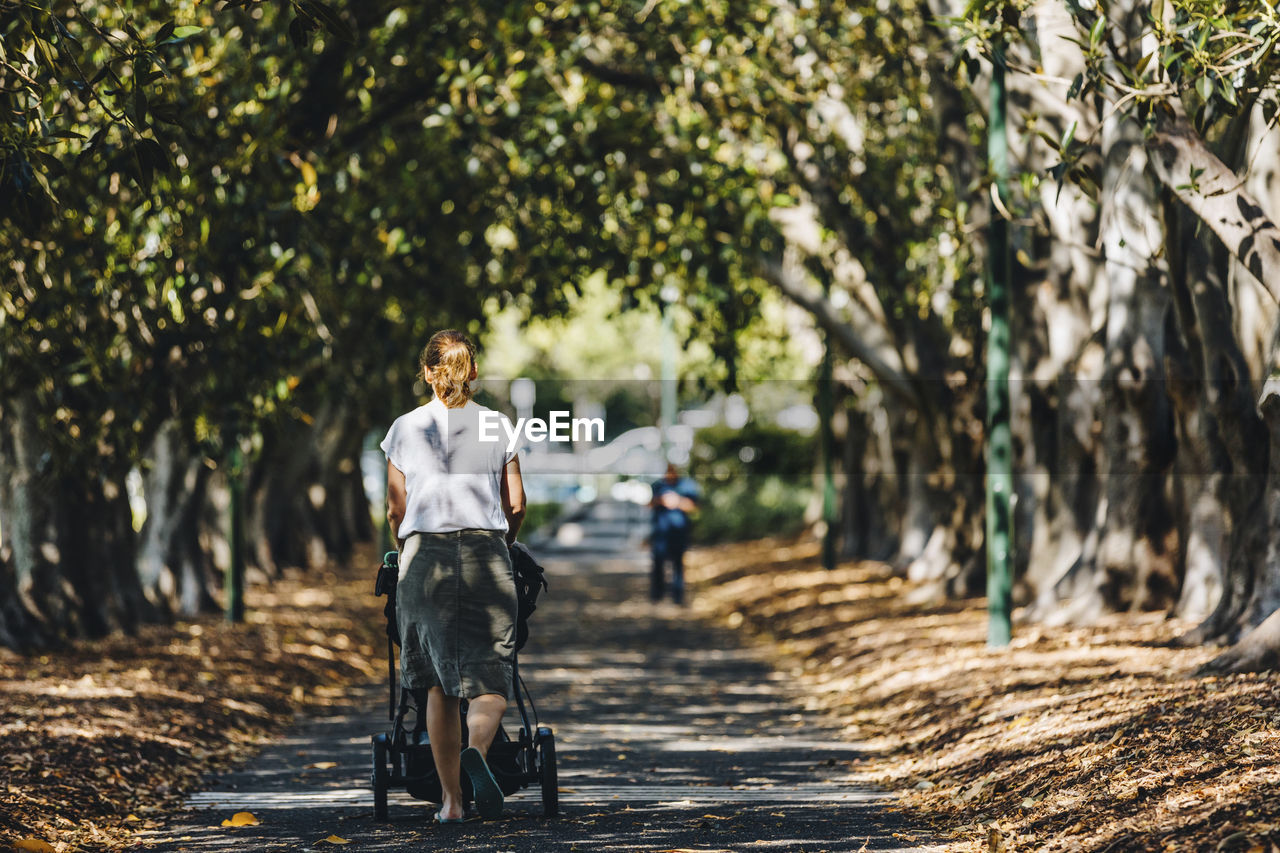 Rear view of woman with baby stroller walking at park