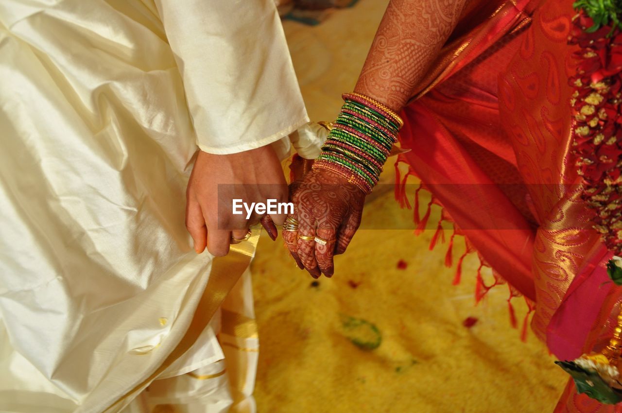 Midsection of indian bridal couple holding hands during wedding ceremony