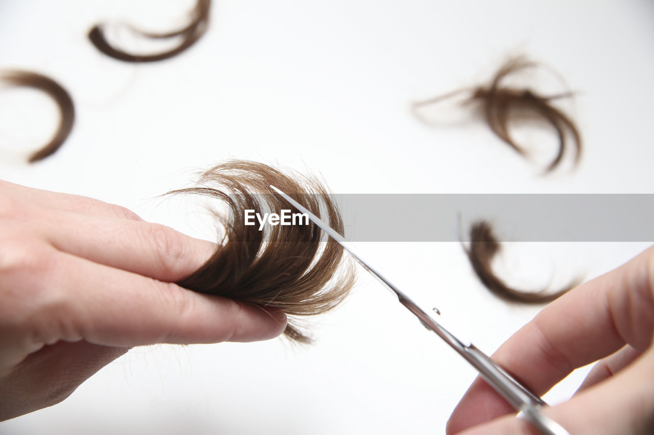 Cropped hands cutting hair against white background