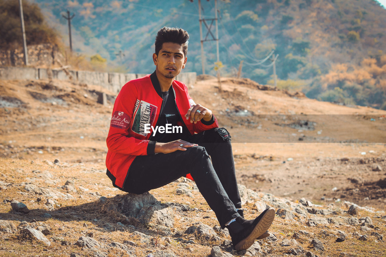 Handsome young man looking away while sitting on rock