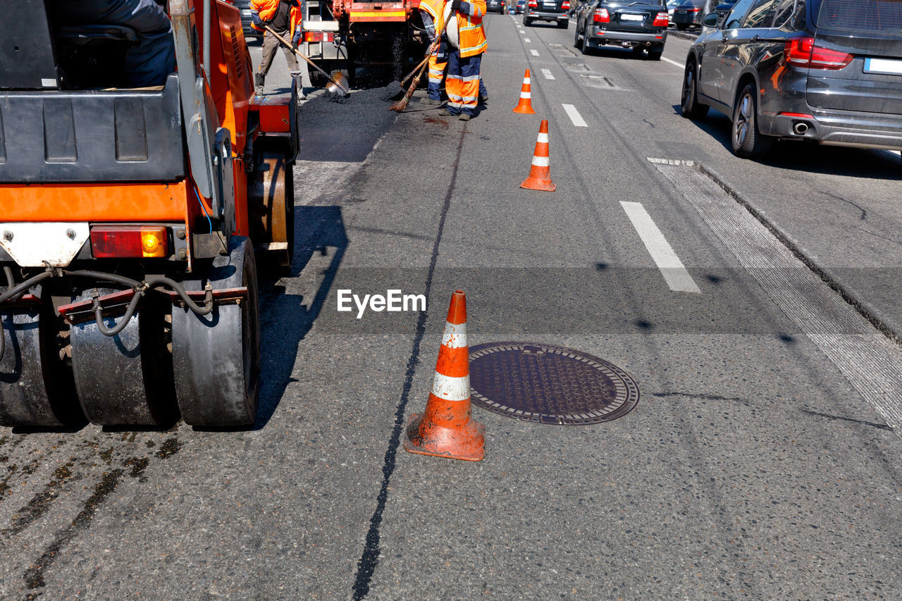 Road orange cones enclose the work crew and road equipment from the carriageway