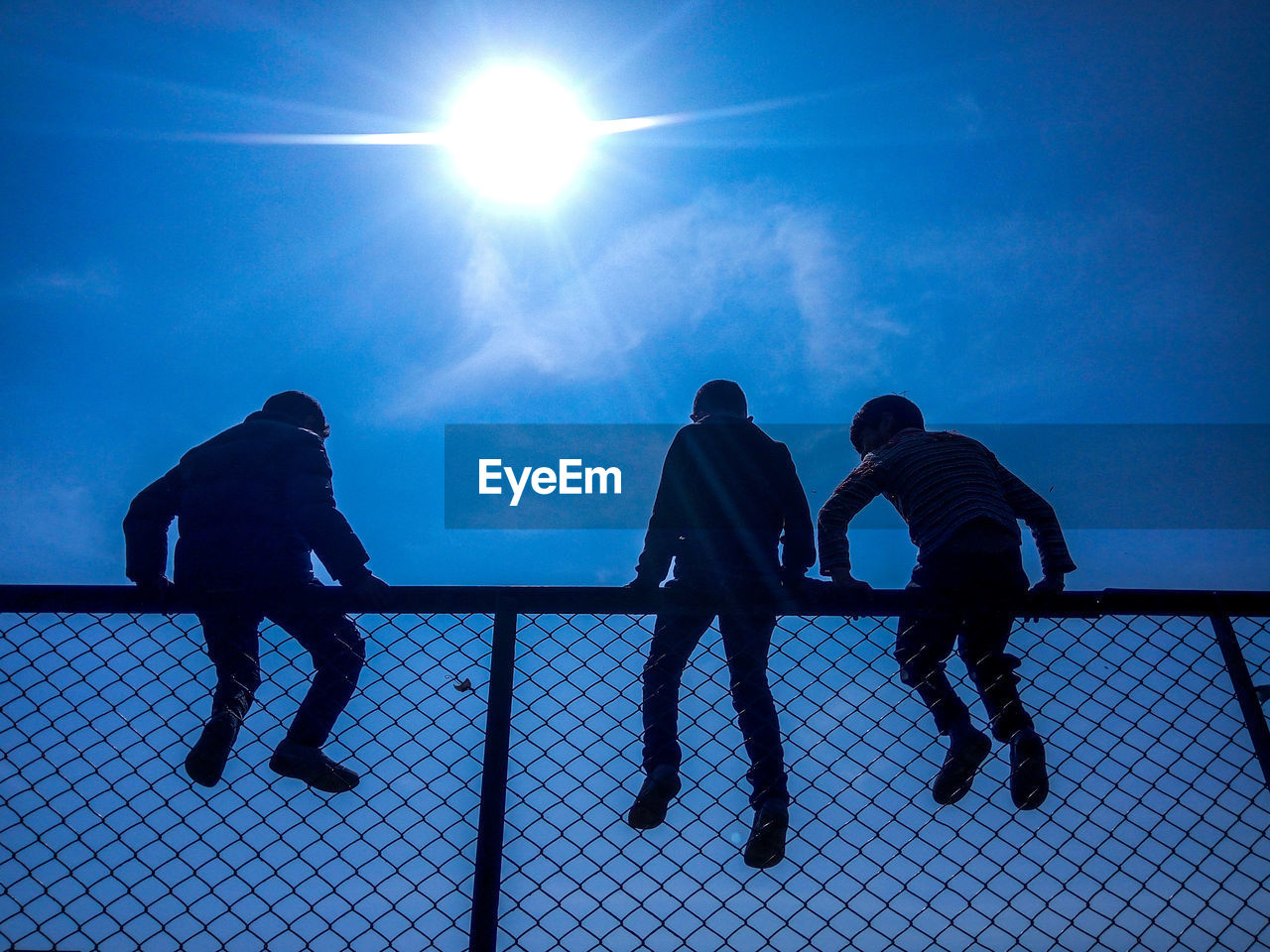 Low angle view of silhouette people sitting on chainlink fence