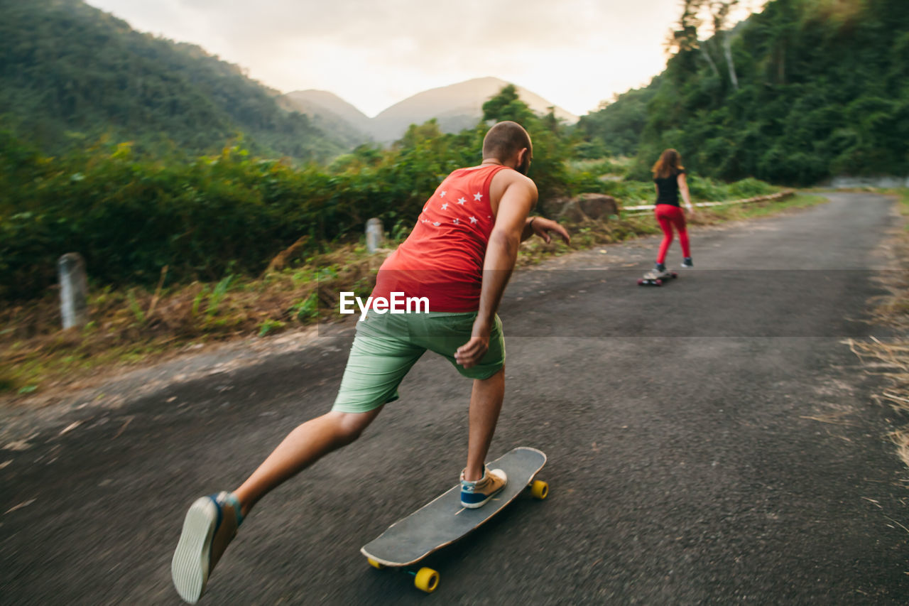 Rear view of people skateboarding on road against mountains