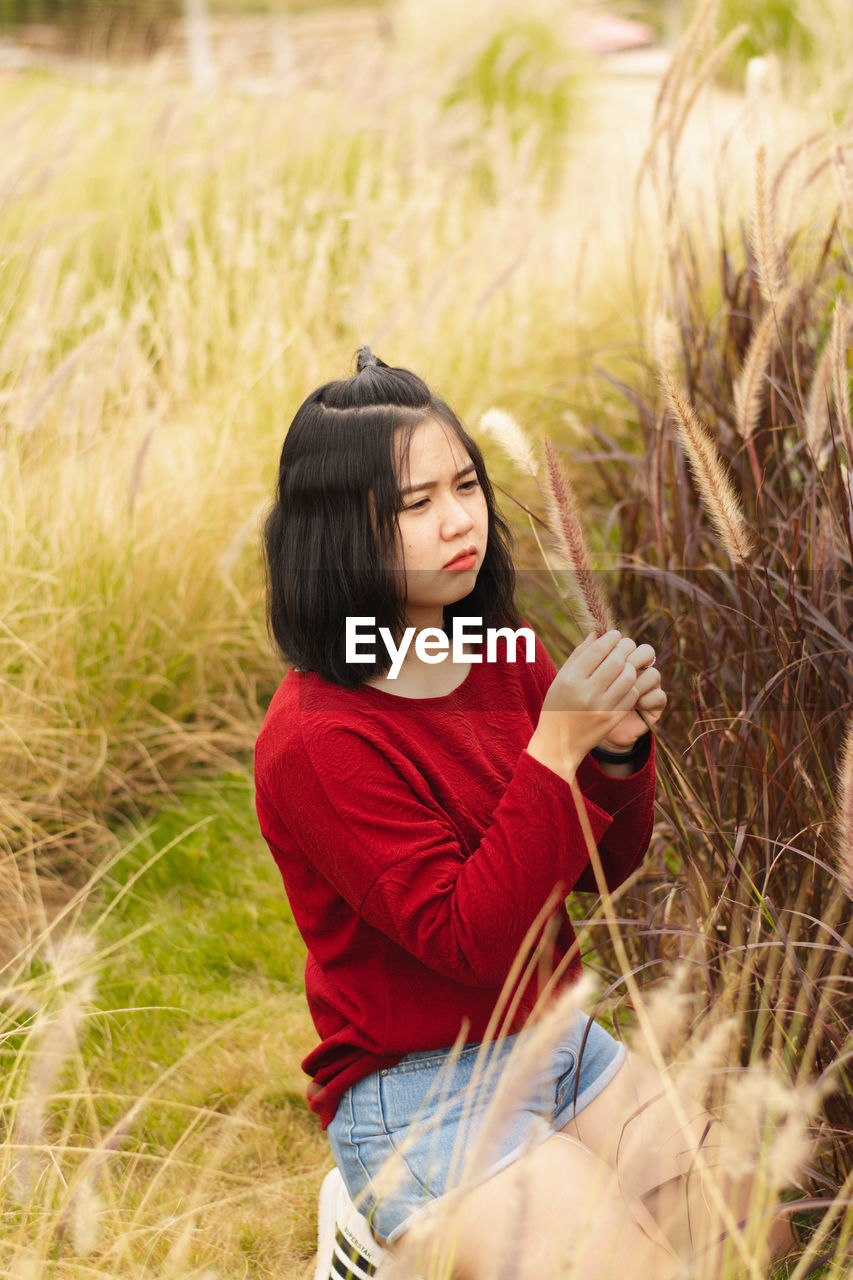 Young woman looking at plant while kneeling on field