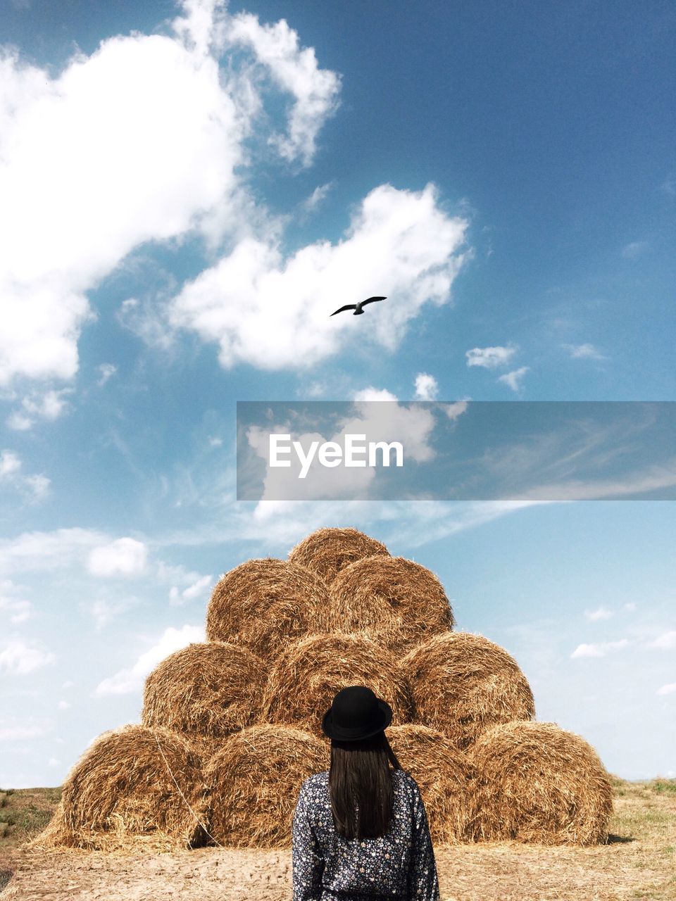 Rear view of woman standing in front of haystack against cloudy sky