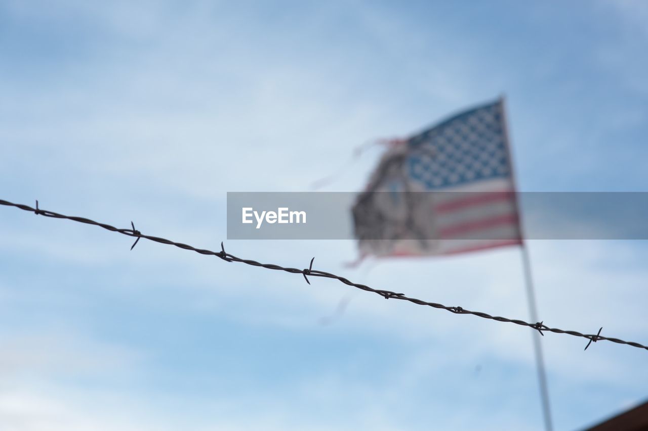 Low angle view of barbed wire fence against american flag