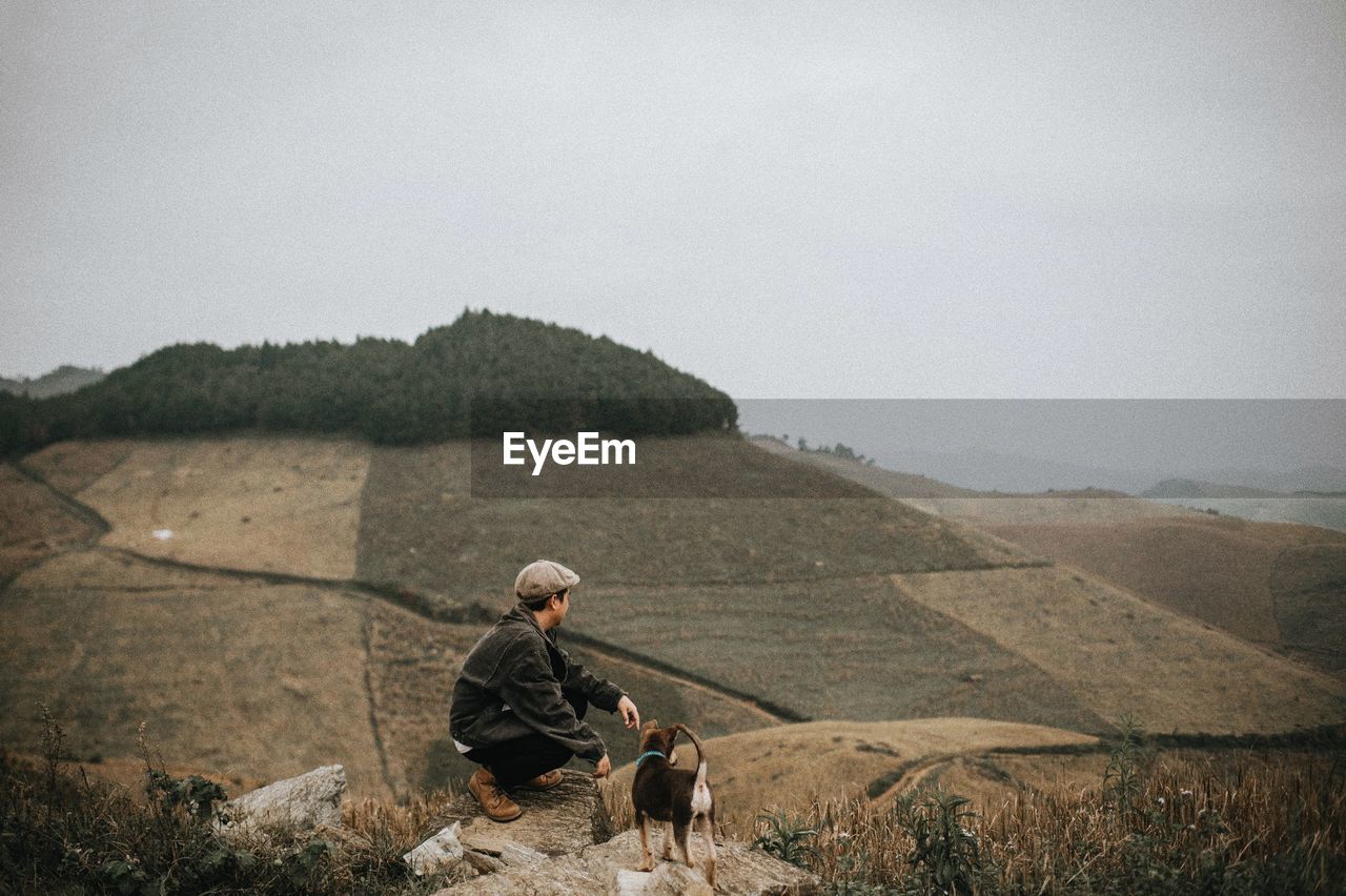 Man and his dog standing on land against sky